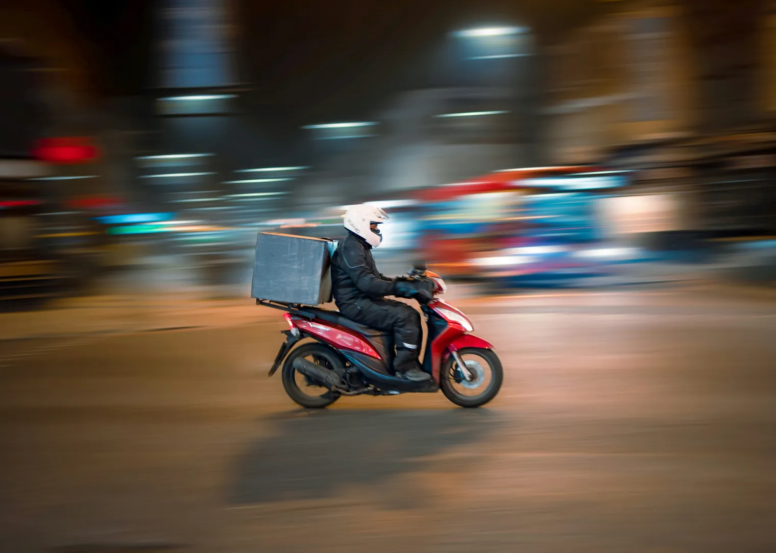 A food delivery rider on a scooter at night with a delivery box