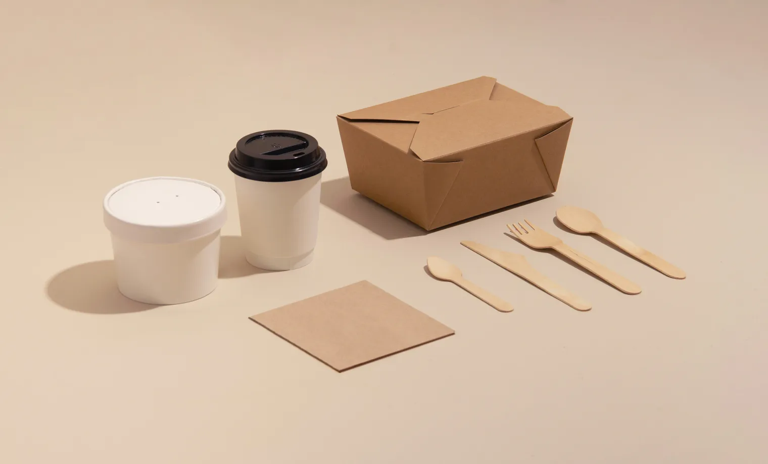 A takeaway coffee, food box and wooden cutlery laid out on a counter